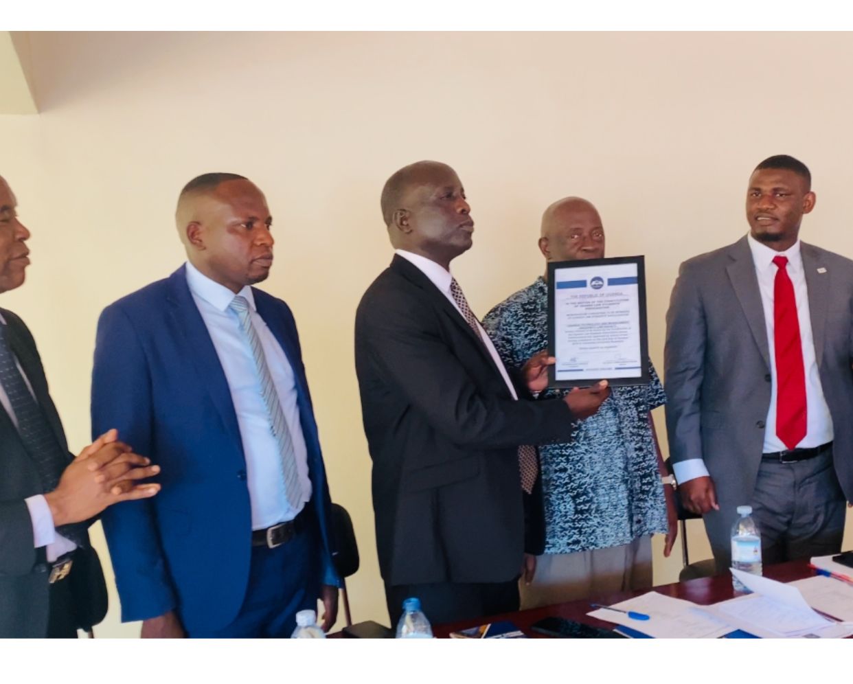 Dr. Wilfred Kokas Aupal and Mr. Duncan Biyinzika on the left receiving a certificate from Counsel Arthur Isiko